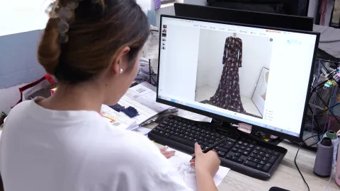 OTO team member sketches a garment beside a dress reference on screen