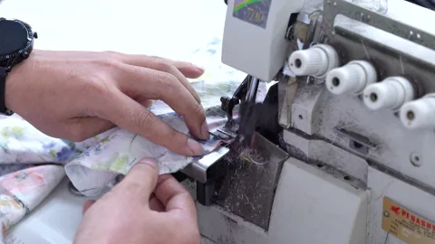Hands guide floral fabric through an overlock sewing machine